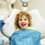 Leczenie kanałowe zębów mlecznych - uśmiechnięty chłopiec na fotelu dentystycznym
