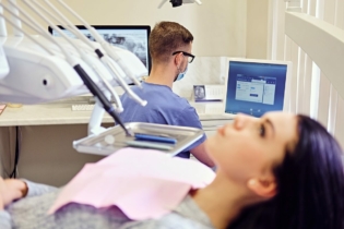 L4 od dentysty - pacjentka na fotelu stomatologiczny i dentysta pracujący przy komputerze