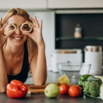 Dieta dla zębów - młoda uśmiechnięta kobieta w kuchni i leżące wokół warzywa i owoce