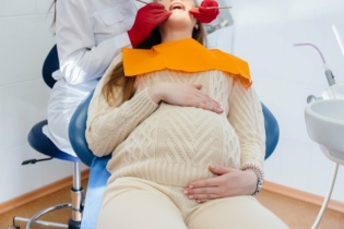 Jak hormony wpływają na dziąsła - kobieta w ciąży na fotelu dentystycznym