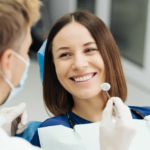 Ekwilibracja zgryzu - uśmiechnięta pacjentka na fotelu stomatologicznym i dentysta trzymający lusterko
